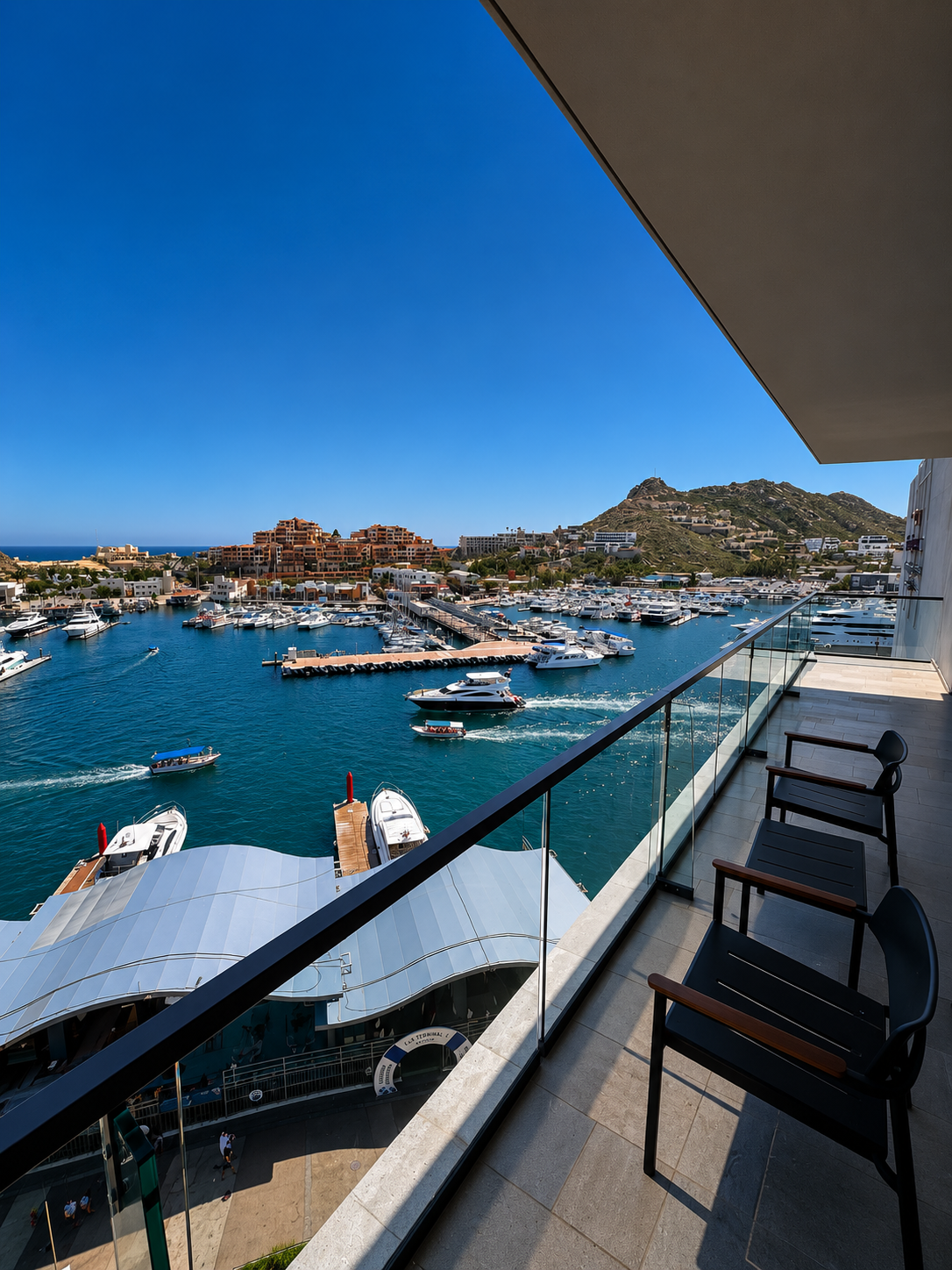 Balcony view over the Cabo San Lucas marina with luxury yachts and hillside resorts under a deep blue sky